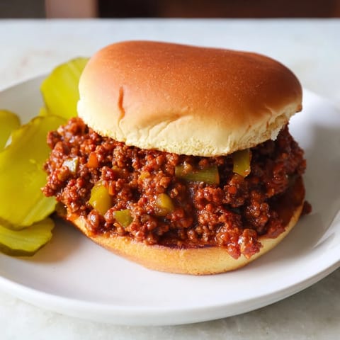 Two soft hamburger buns are stuffed with a saucy beef Sloppy Joe mixture, dotted with chopped onion and green bell pepper.