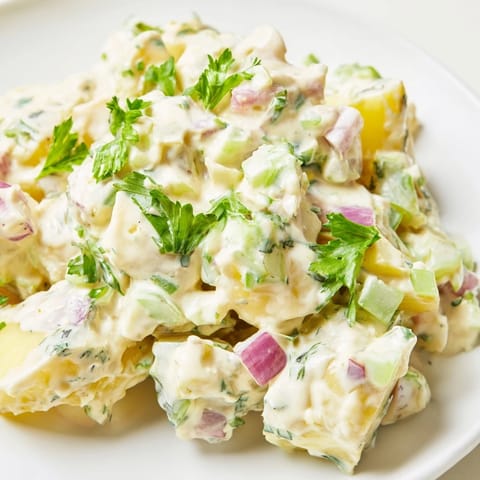 Chilled potato salad served in a white bowl, garnished with chopped parsley and hard-boiled eggs.