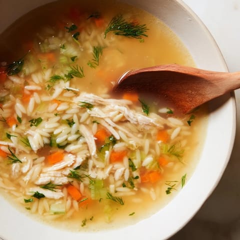 A steaming bowl of homemade Chicken Lemon Orzo Soup garnished with fresh dill and lemon slices.  
