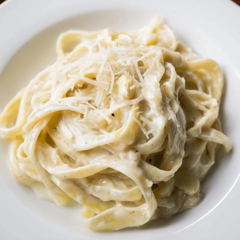 Fresh fettuccine noodles glisten with velvety roasted garlic cream sauce and a generous snowfall of Parmesan cheese.