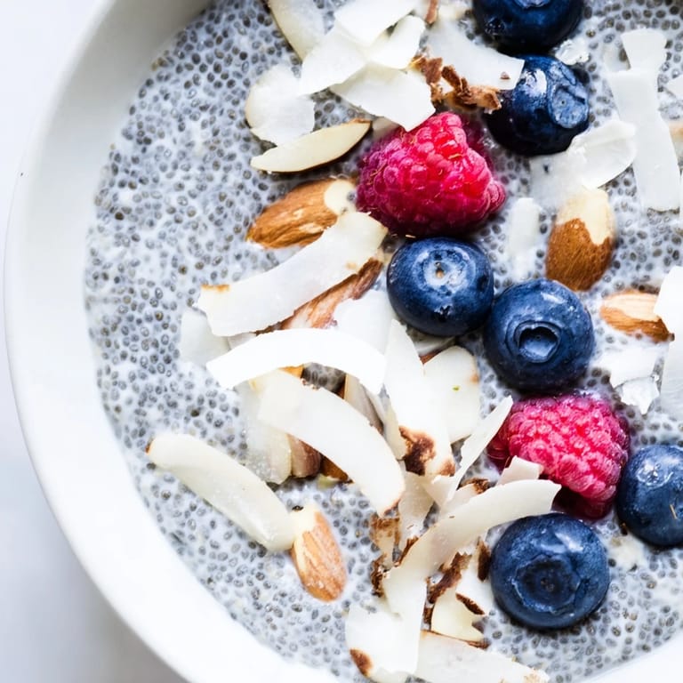 Overnight poppy seed chia pudding in a white bowl, stirred to a smooth texture with a spoon and coconut flakes.
