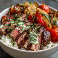 Grilled Steak Bowl topped with vibrant chimichurri sauce over fluffy rice and colorful roasted vegetables.