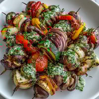 Colorful grilled vegetable skewers with chimichurri sauce, featuring vibrant summer veggies and fresh herb dressing for a healthy BBQ side.  